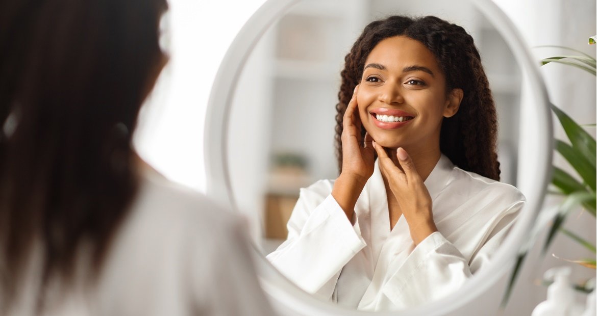 Mulher afro-americana toca seu rosto sorrindo ao observar sua pele lisa do rosto